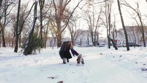 Cute dog running behind lady and playing in snow.