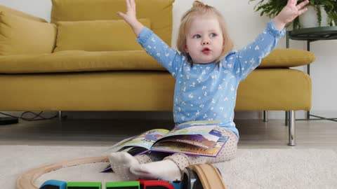 A Little Girl With A Book On Her Lap Flopping Her Hands