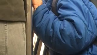 Little boy in blue jacket licks subway rail