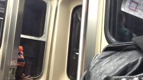 Man in orange and black beanie smokes on the back of subway train