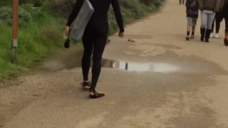 Wet suit flippers guy walks down road with surboard