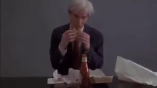 Watch Artist Andy Warhol indulging in a juicy hamburger.