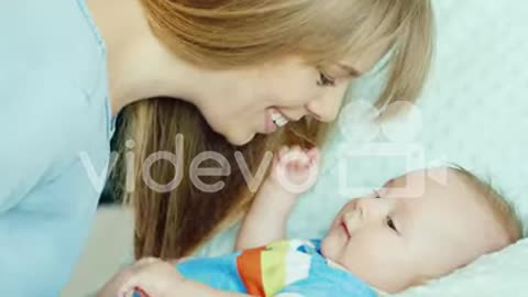 Happy Young Mother Looking At Her Child Holding His Pen The Baby Lies In The Crib