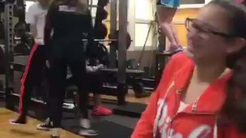 Blue shorts girl tries to hang from squat rack but falls down