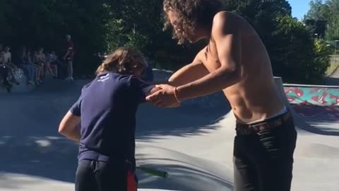 Shirtless curly hair guy kicks up skateboard skateboard hits scooter kid on head
