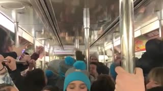 Subway train filled with college students wearing gray and blue beanie singing song