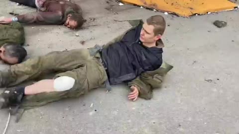 A Russian POW is dragged on the floor like a corpse and laid beside two Russian corpses