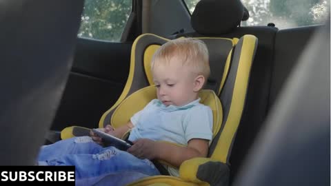 Cute toddler baby boy sitting in car seat and watching a video from smart-phone