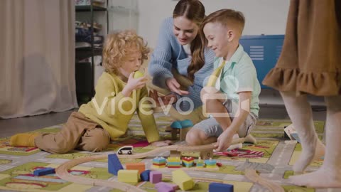 Children Playing With Cars And Pieces Of Wood Sitting On A Carpet In A Montessori School