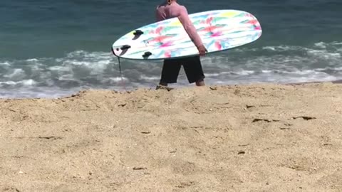 Guy in pink shirt carrying blue surf board