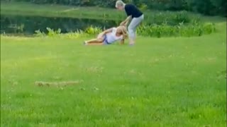 Dogs runs in grass to couple knocks over blonde lady in white