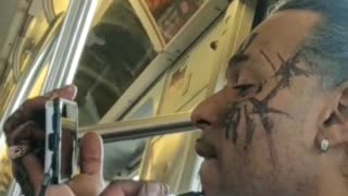 Guy draws on his face with a sharpie and uses his cell phone a a mirror, on metro
