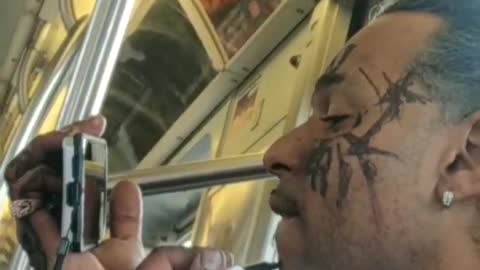 Guy draws on his face with a sharpie and uses his cell phone a a mirror, on metro