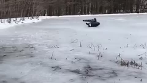 Man sleds across frozen lake in a black tube pulled by truck