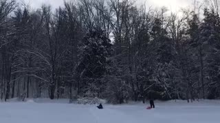 Green jacket on blue innertube rides down snow bank