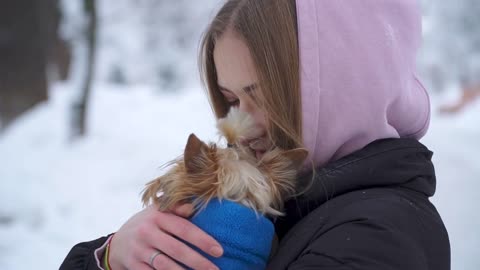 Portrait of girl hugging small dog covered in blanket close up outdoors. Yorkshire terrier is cold