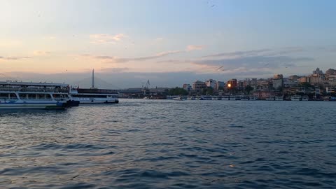 Calm sea waves at sunset, with birds, ships and distant buildings at the bridge