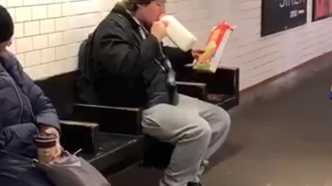 Guy drinks milk and pours cereal into his mouth in subway station