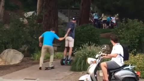 Guy on hoverboard helping guy on skateboard