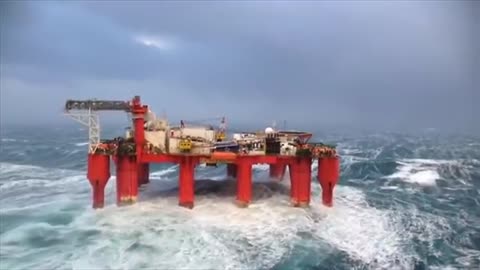 Huge waves crash against swaying North Sea oil rig