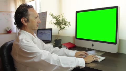 Man in his home office typing on a keyboard, green screen computer display. Free