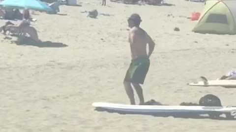 Man in green shorts on the beach does stretches