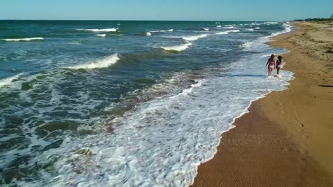 Girls walking on the sand next to the sea waves