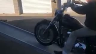 Guy drives motorcycle up ramp onto pick up truck, tips over and falls