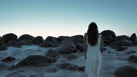 Woman walking on beach towards boulders