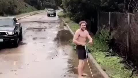 Shirtless guy in black shorts wakeboarding on flooded streets falls immediately