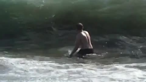 Guy in black shorts gets knocked down by wave