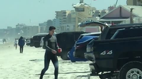 Guy wearing wetsuit walking back to truck with red cup in hand