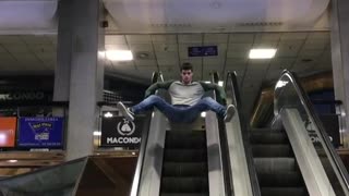 Guy in grey baseball shirt slides down escalator