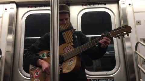 Guy plays guitar and pan flute on subway train