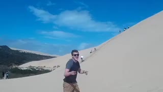 Sunglasses guy surfs down sand dune and faceplants