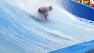 Long haired man falls off artificial surf machine