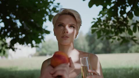 A Woman Holding a Glass of Champagne Getting an Apricot from a Person's Hand