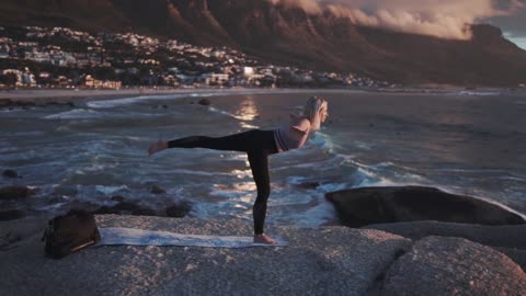 Slow Motion Footage Of A Woman Doing Yoga Outdoors With The View Of A Village By Sea
