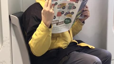 Yellow jacket man reads newspaper very close to face on subway