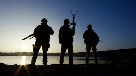 Soldier silhouettes posing with guns in the sunset
