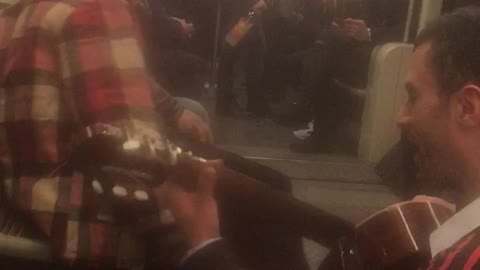 Man in red flannel and man with guitar singing on train