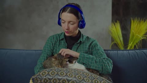 Beautiful young calm female pet owner in wireless headphones sitting on couch