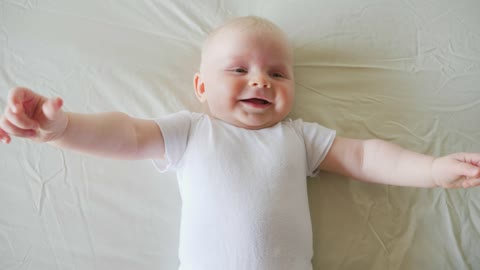 Happy baby lying on white bed in white shirt