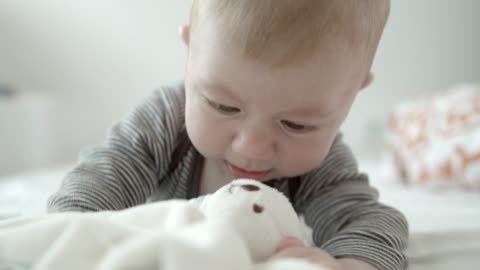 Cute baby playing with a teddy Baby in bed biting and playing with a stuffed animal.