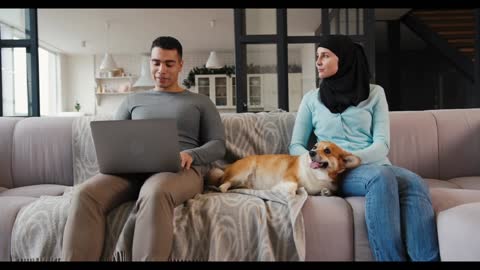 Muslim woman in hijab plays with cute corgi puppy near husband