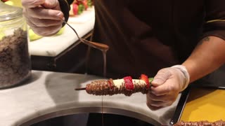 Covering fruit on sticks with chocolate.