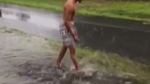 A guy in flannel shorts swims in puddle next to street