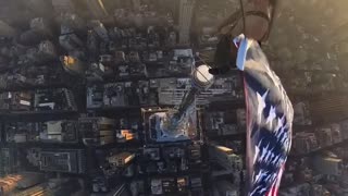 Guy waving American Flag at the top of a building.