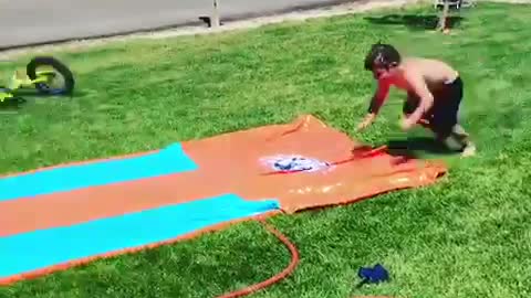Shirtless kid runs across grass and slides on slip and slide face down