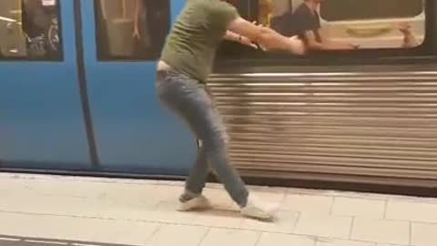 Man in green pretends to stop subway train with hands